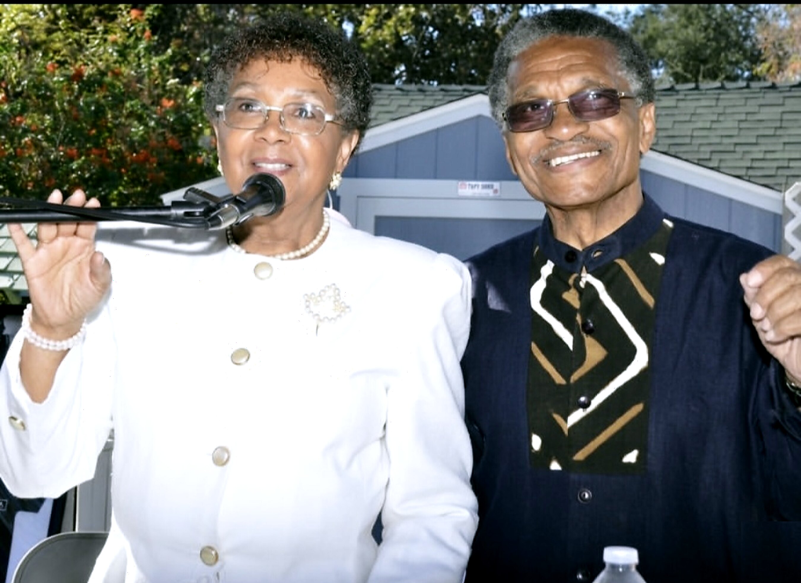 Joe and Ruthie Hopkins together at an outdoor event, Ruthie speaking at a microphone.
